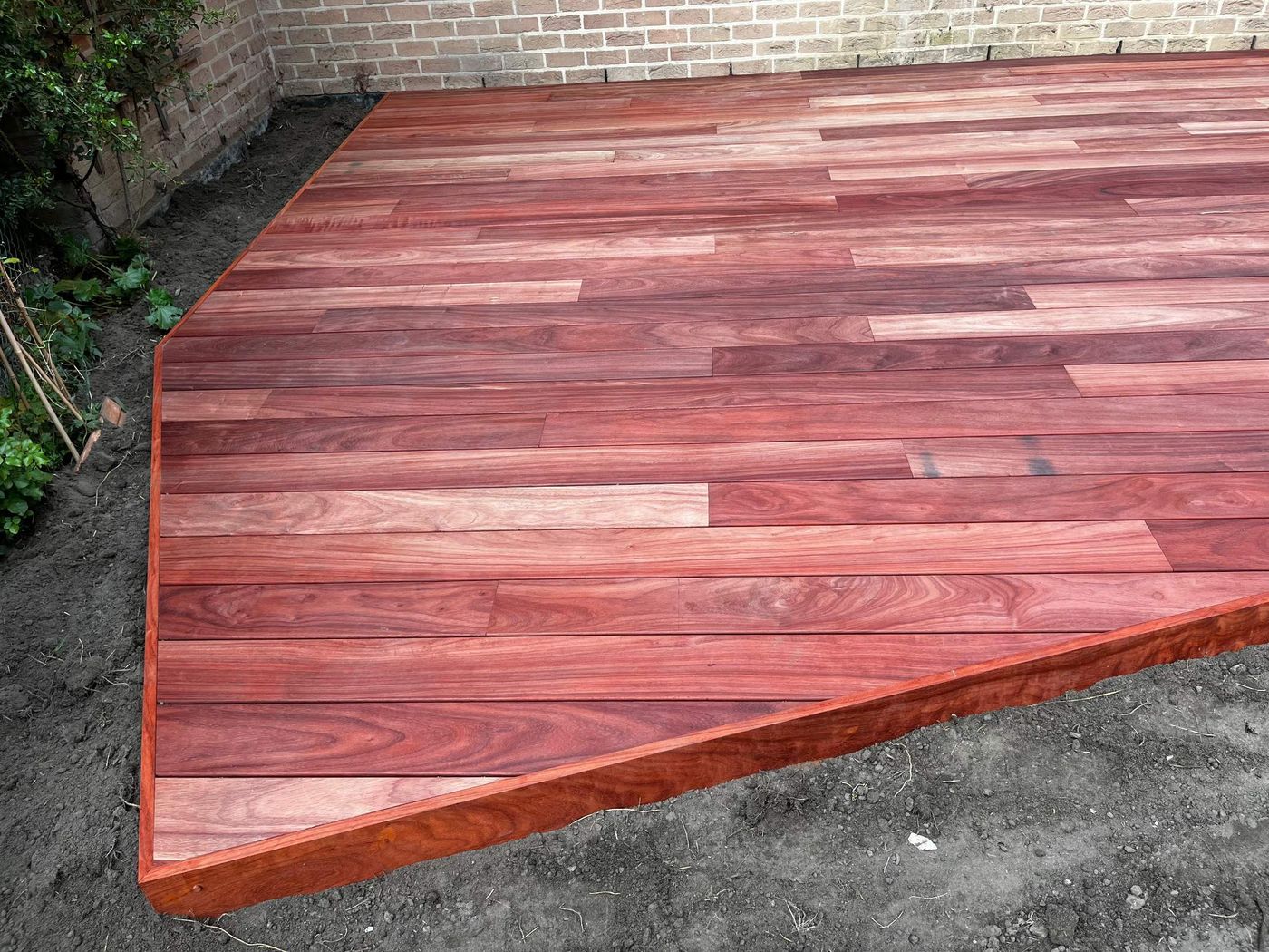 Parquet de jardin VETEDY en padouk aux angles coupés, le long d'un mur en briques